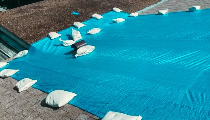 Blue tarp installed with sandbags on a roof to represent the keyword emergency shingle roof repair.