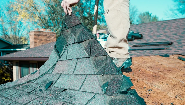 Man removing shingles from a roof to represent the keyword full roof replacement.