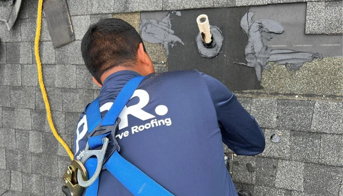 Man working on a roof next to a metal pipe to represent the keyword shingle roof systems.