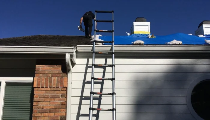 Metal ladder leaning against a house where a blue tarp with sandbags is installed to represent the keyword best roof tarp.