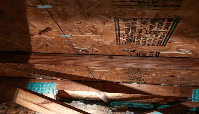 Interior view of an attic showing the underside of OSB sheathing with manufacturer stamps, providing a technical look at what is radiant barrier roof decking during house construction.