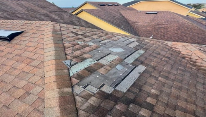 A close-up view of a house roof with missing shingles and exposed underlayment, showing why homeowners need to know how to protect your roof from storm damage.