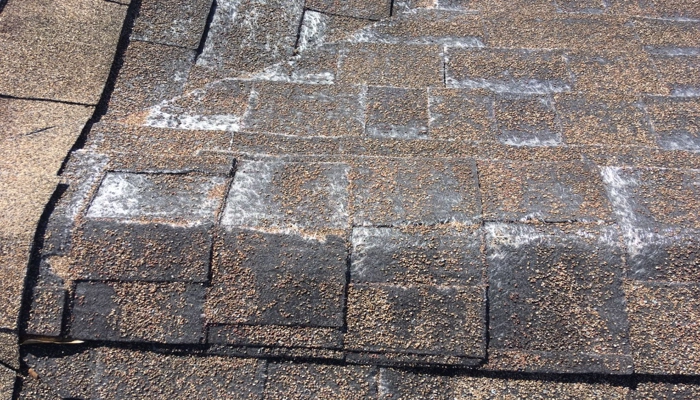 Close-up of damaged asphalt shingles with significant granule loss and exposed fiberglass, a key indicator for homeowners wondering "how old is my roof" and if it needs replacement.