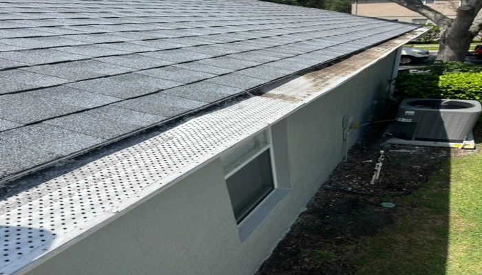 Close-up of grey asphalt shingles on a Florida home with a perforated gutter guard system, illustrating the common choice when evaluating metal roof vs shingles in Florida for budget-conscious homeowners.